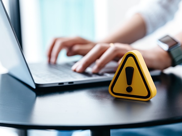 yellow exclamation mark next to person typing on laptop